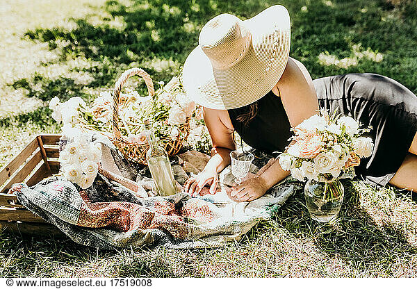 Woman lays on blanket surrounded by picnic flowers and wine