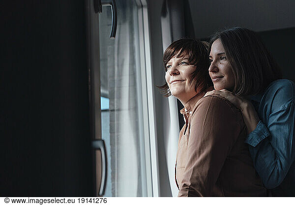 Woman leaning on lesbian friend shoulder near window at home