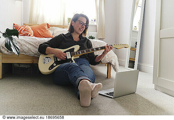 Woman learning guitar watching tutorial on laptop at home