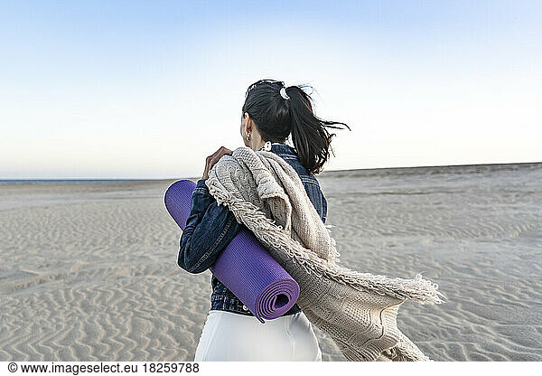 Woman leaving the beach while carrying her mat