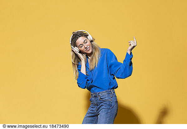 Woman listening music and dancing against yellow background