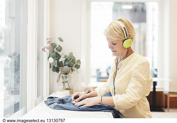 Woman listening music while attaching brooch on denim jacket at cafe