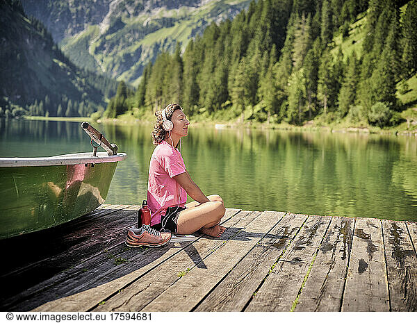 Woman listening musing through headphones sitting on jetty