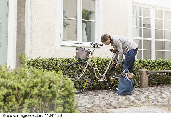 Woman locking bicycle by plants outside house