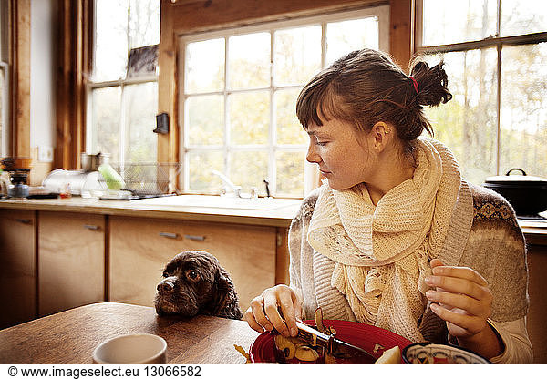Woman looking at dog while cutting fruits at table in home
