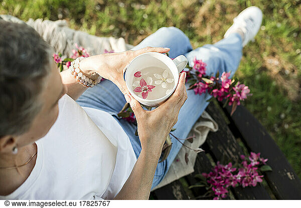 Woman looking at flower floating on water in cup at garden