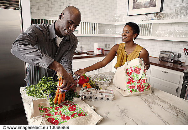 Woman looking at husband putting vegetables on kitchen island