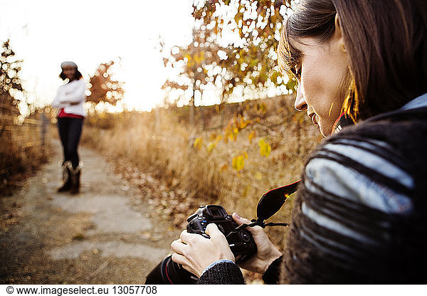 Woman looking at photographs in digital camera while friend posing on footpath