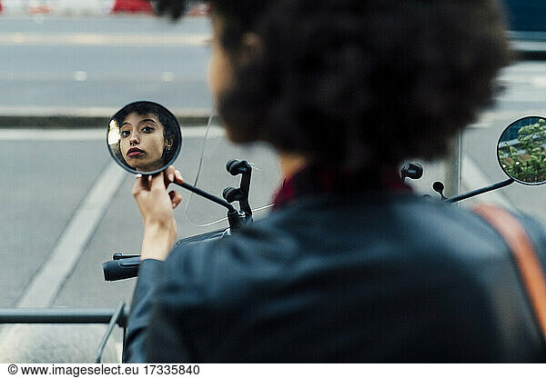 Woman looking at side-view mirror of motor scooter