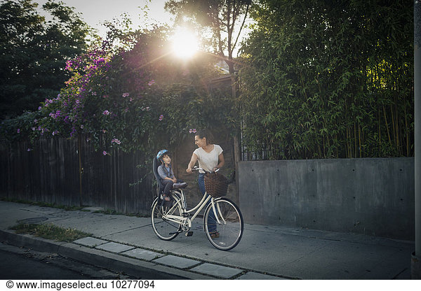 Woman looking at son sitting on bicycle back seat outdoors