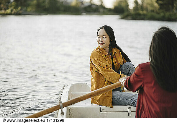 Woman looking away while female friend rowing boat on lake
