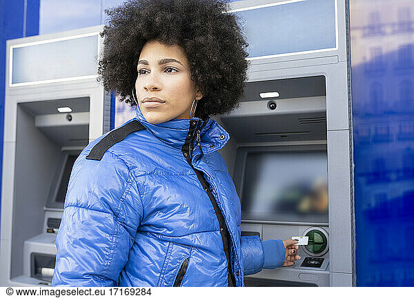 Woman looking away while removing ticket from machine at bus stop