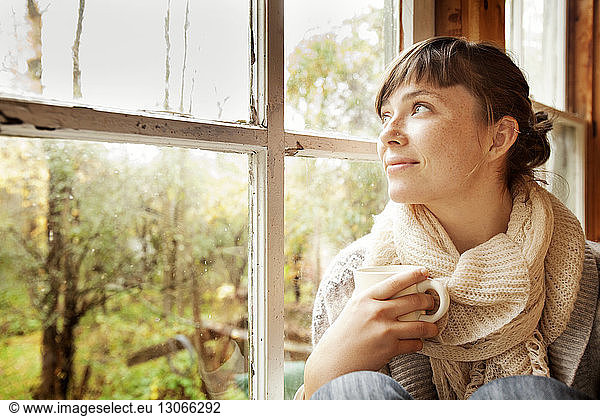 Woman looking away while sitting by window at home