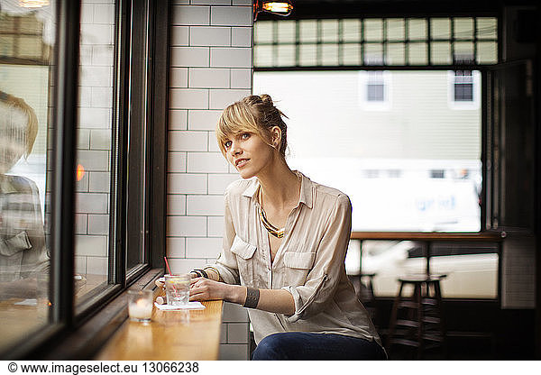 Woman looking away while sitting on stool in bar