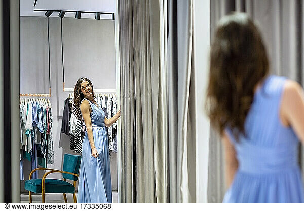 Woman looking in mirror while wearing blue dress in boutique