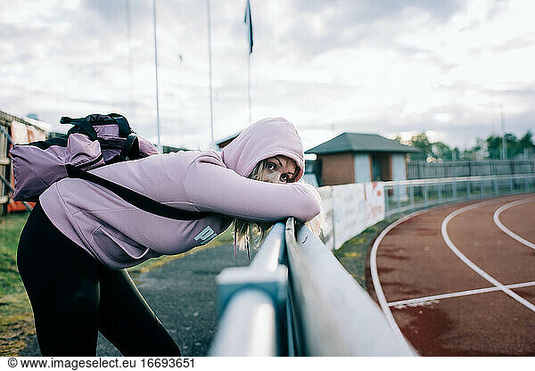 woman looking nervous stood by a running track waiting