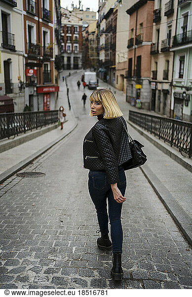 Woman looking over shoulder walking on street in city