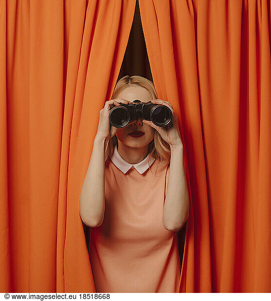 Woman looking through binoculars amidst orange curtains