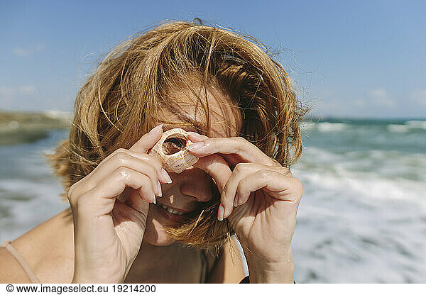 Woman looking through shell at beach