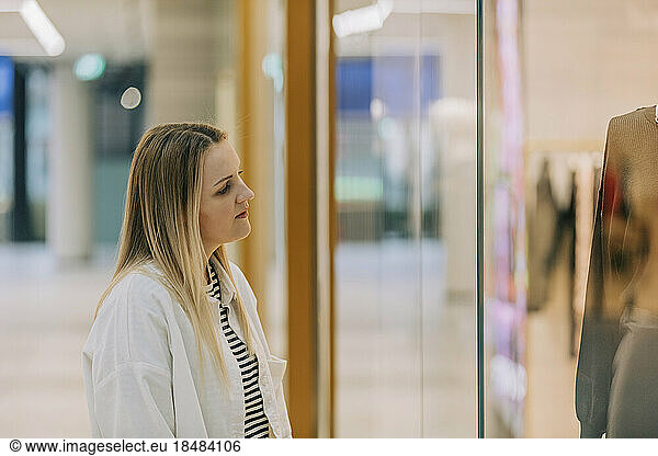 Woman looking through store window at mannequin in shopping mall