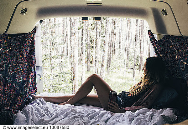 Woman looking through window while relaxing in camper van