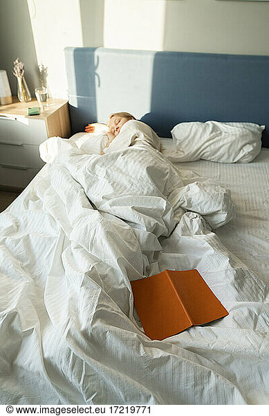 Woman lying by book in bed at home