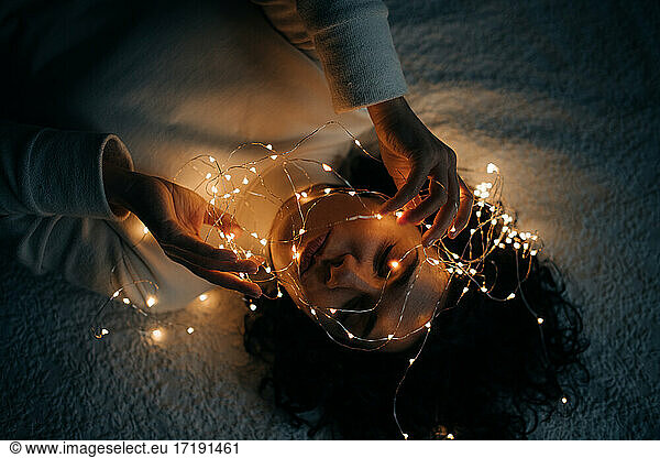 Woman lying down in bed with tangled string lights in her hair