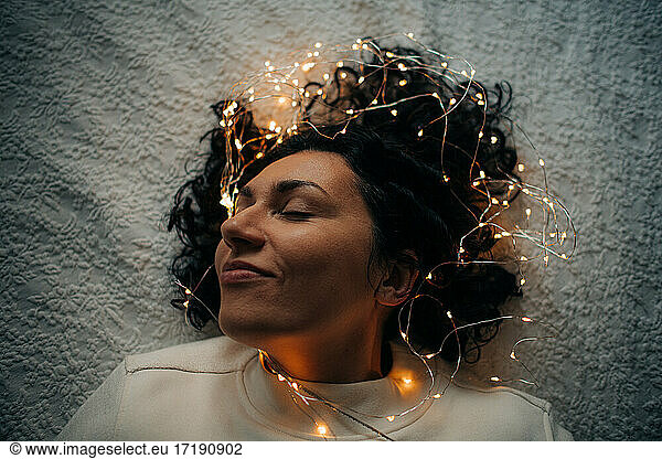 Woman lying down with tangled string lights in her hair  smiling
