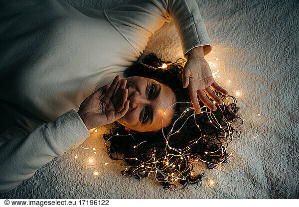 Woman lying down with tangled string lights in her hair smiling