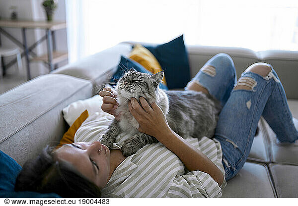 Woman lying on sofa and stroking cat at home