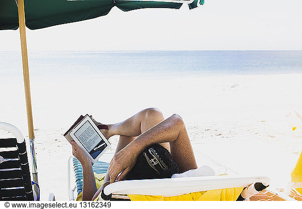 Woman lying on sun lounger  reading e-book