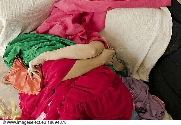 Woman lying under heap of clothes at home