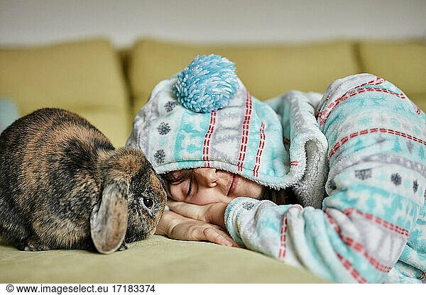 Woman lying with eyes closed next to brown pet house rabbit