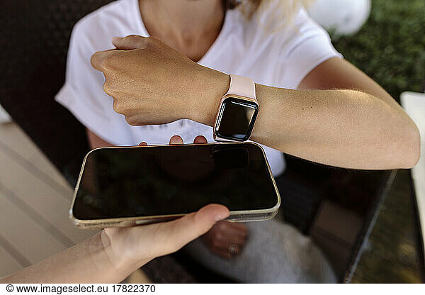 Woman making contactless payment through smart watch on mobile phone held by cashier