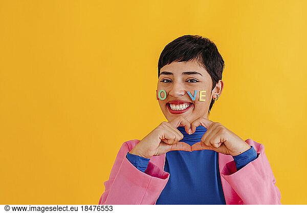 Woman making heart shape gesture against yellow background