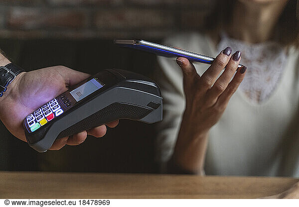 Woman making payment through mobile phone at cafe