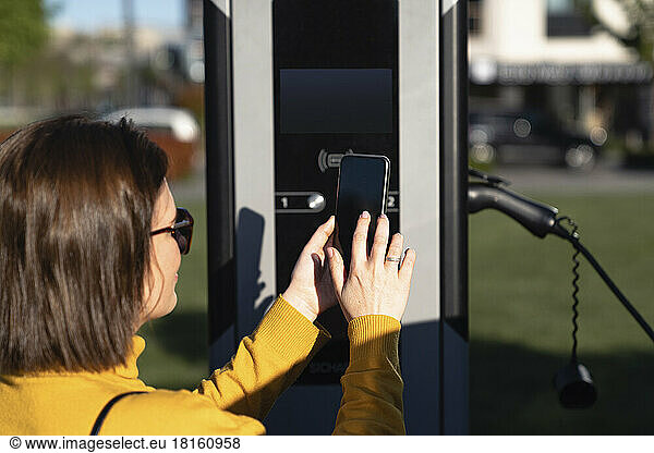 Woman making payment through smart phone at vehicle charging station