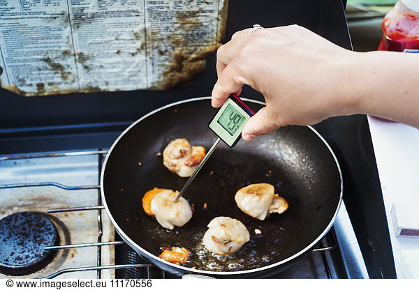 Woman measuring the temperature of a scallop in a frying pan with a digital thermometer.