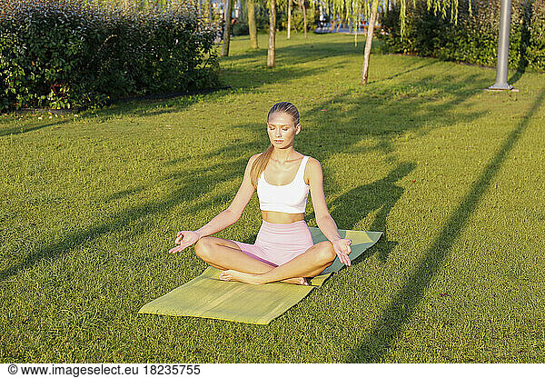 Woman mediating on exercise mat in park