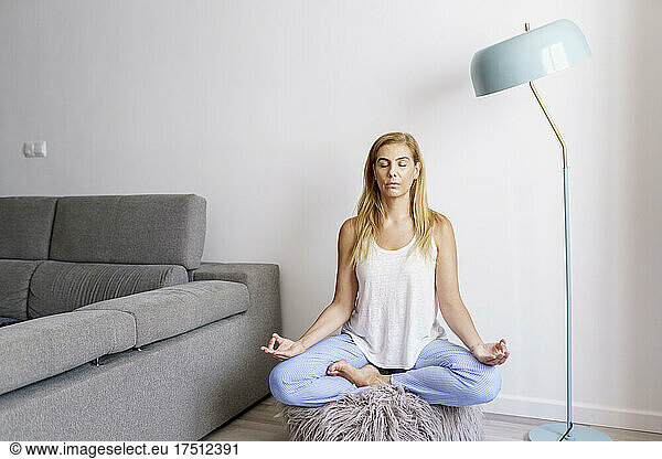 Woman meditating against wall in living room at home