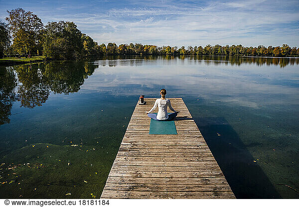 Woman meditating in front of lake under sky