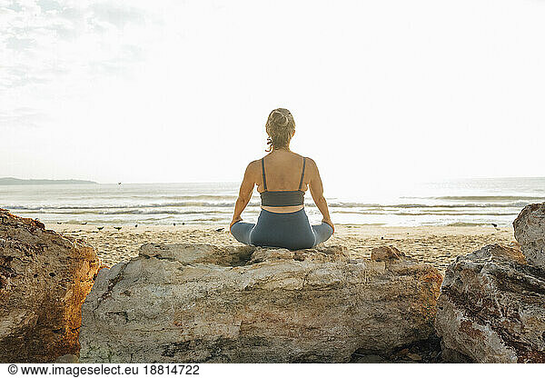 Woman meditating on rock at beach