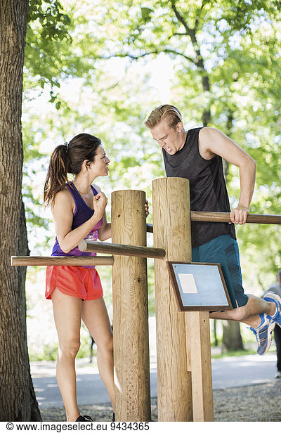 Woman motivating man in doing chin-ups on wooden bars at outdoor health club