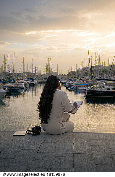 Woman on her back working seated overlooking a harbor