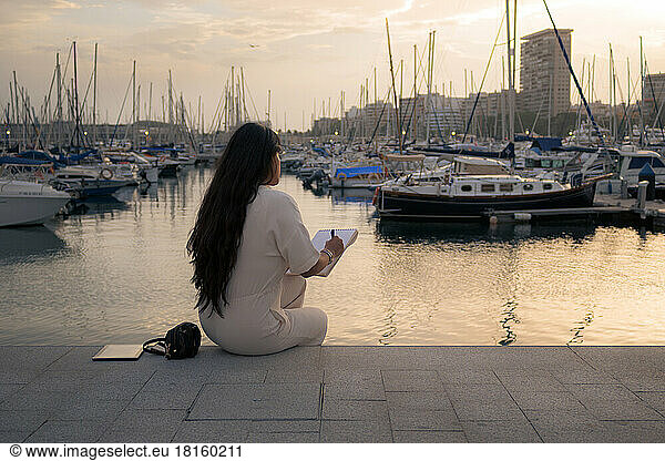 Woman on her back working seated overlooking a harbor