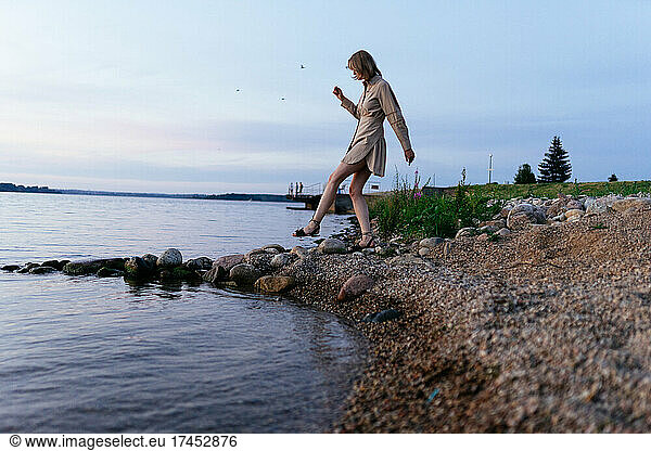 Woman on the shore of the lake in a summer dress  steps on the stones