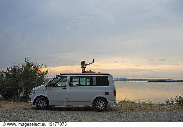 Woman on top of the van making a selfie at sunset on the lake