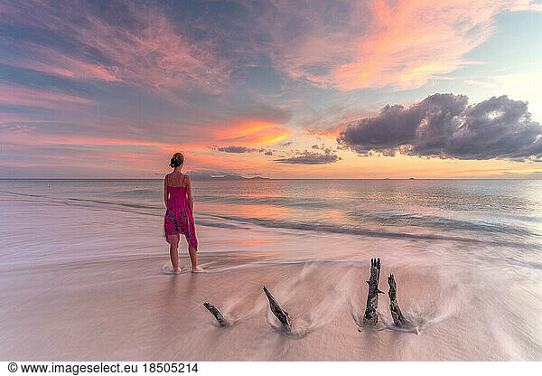 Woman on tropical beach looks at Caribbean sea at sunset