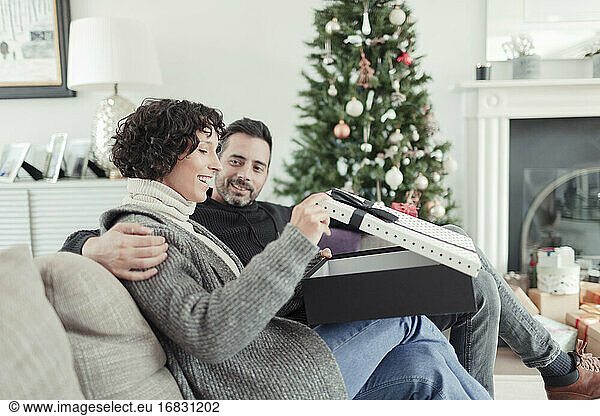 Woman opening Christmas gift from husband on living room sofa