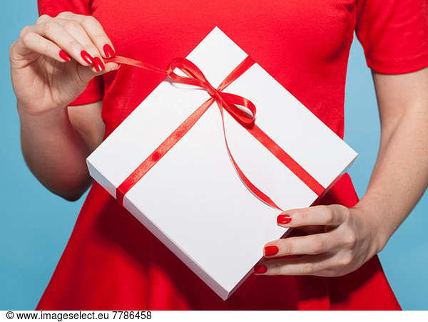 Woman opening white gift box with red bow  mid section
